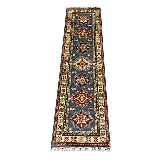 This natural-dyed wool runner features a blue field with a row of bold Kazak-style geometric medallions. Deep red and navy...