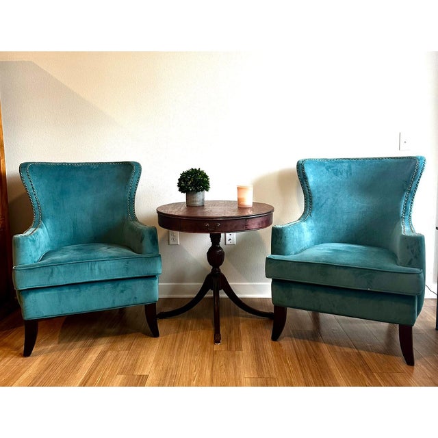 Elegant pair of teal velvet wingback accent chairs featuring a beautifully curved silhouette and classic nailhead trim....