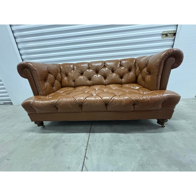 Offered is an iconic tufted brown leather loveseat sofa set on brass casters by Cocheo Brother NYC. This piece is all...
