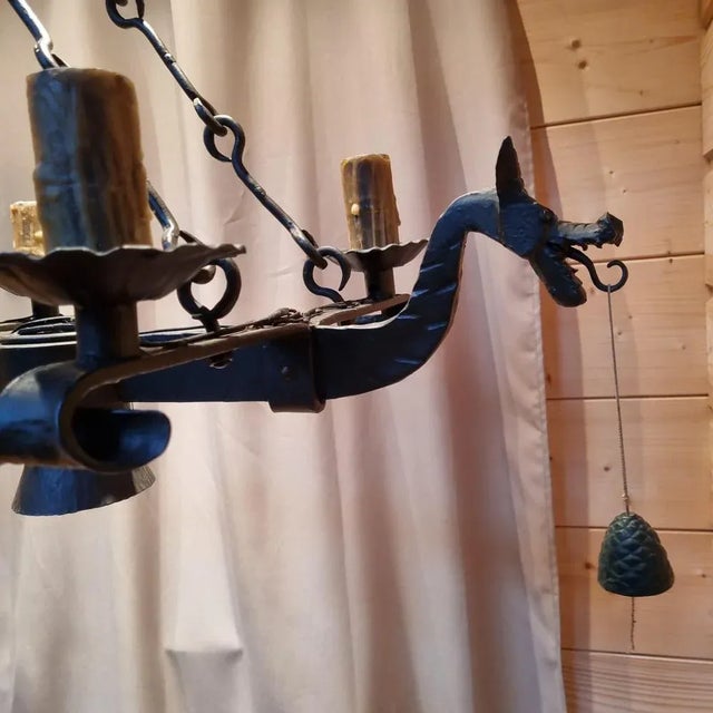 Wrought iron chandelier with 6 cups and wax lamp. At each end a dragon head holding a cord in its mouth with a bell at the...