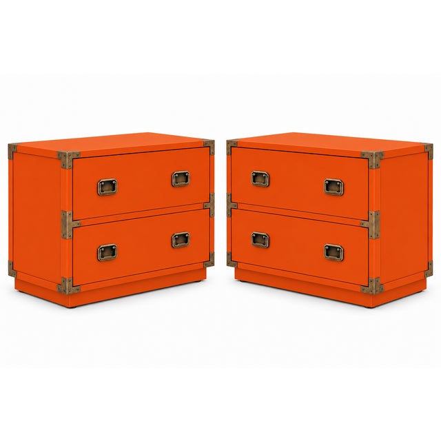 A striking pair of campaign-style nightstands with a vivid orange finish and warm brass-tone hardware. Each nightstand has...
