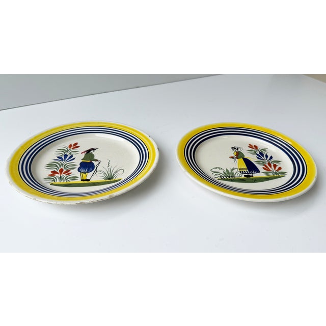 A pair of antique plates with hand painted designs of a Breton man and woman. Each marked "Henriot Quimper France 12"
