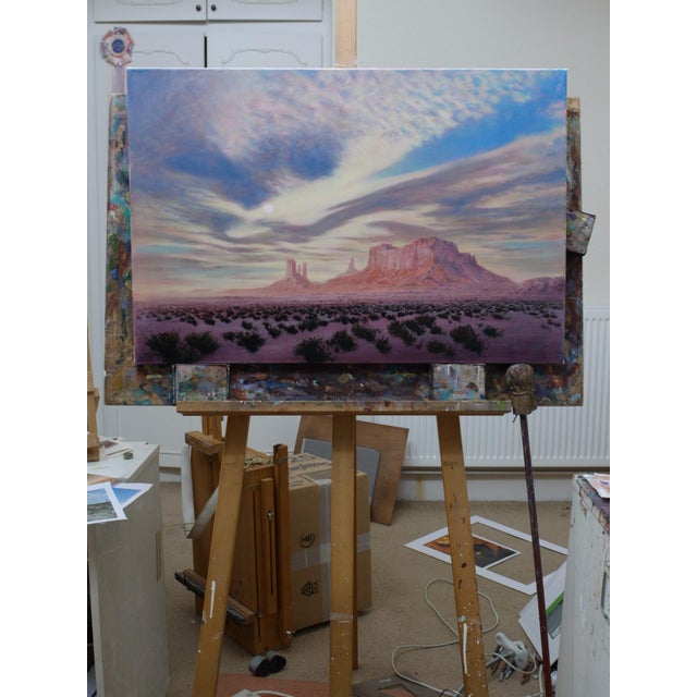The painting depicts a vast desert landscape, featuring dramatic rock formations that rise majestically against a sky...