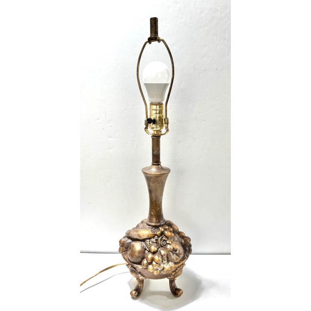 A substantial 1980s cast metal table lamp featuring a sculptural fruit bowl motif resting on three small feet. The warm...