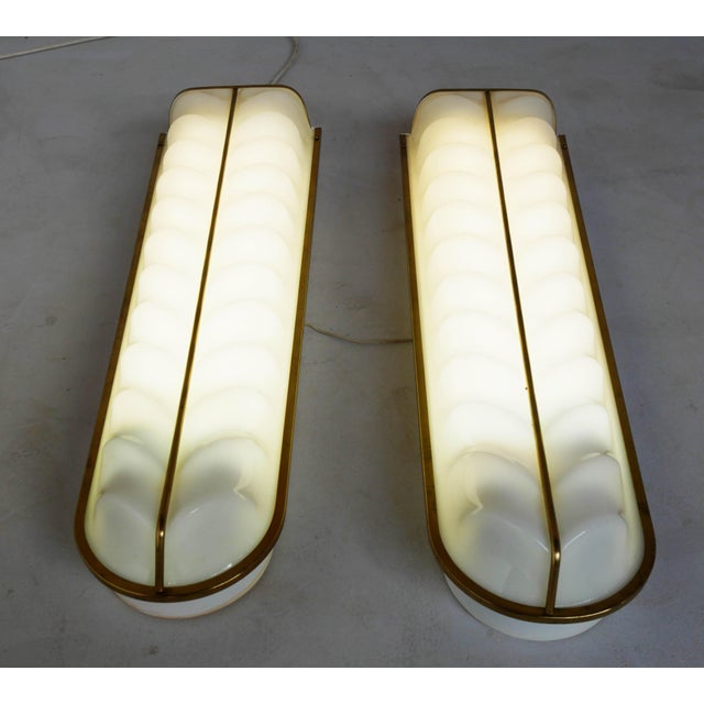 Pair of white opal acrylic glass wall lamps with brass trim, metal frame, and fluorescent tube lighting. There are two...