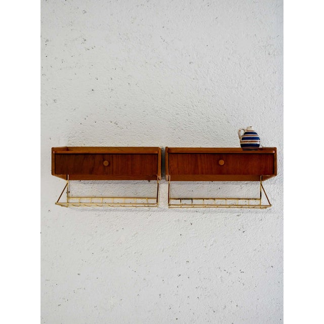Pair of suspended teak bedside tables with brass structure and drawer. Light and geometric design, typical of the 1950s....