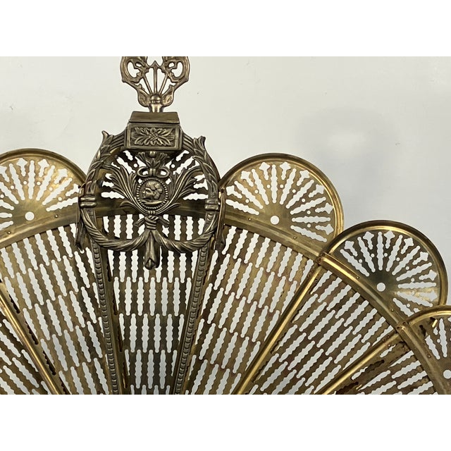 Antique brass folding fireplace fan screen, featuring pierced brass panels and a classical draped motif at the top center....