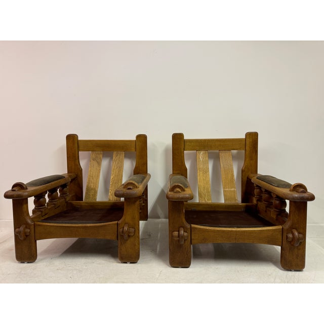 A pair of sculptural mid-century armchairs in solid oak, reflecting a strong Brutalist influence in both form and...