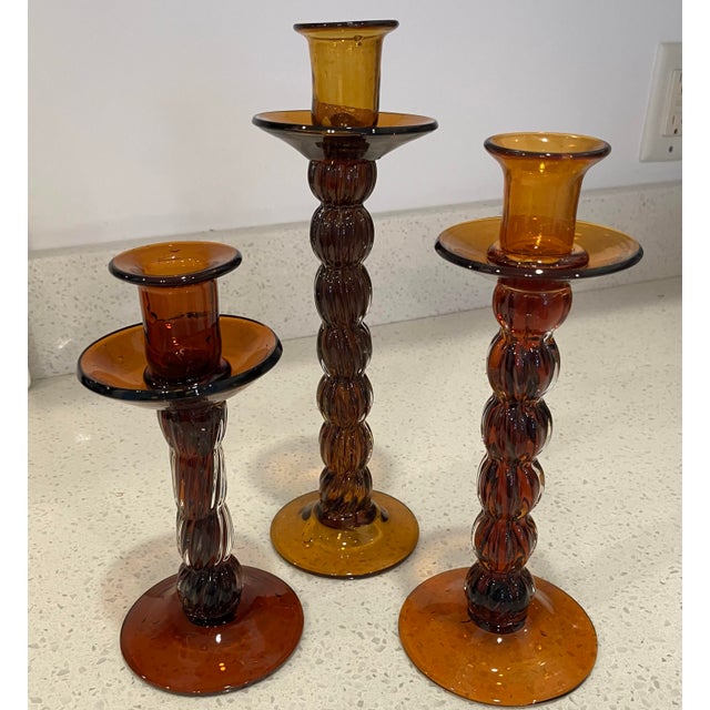 Set of three amber colored er colored glass candlesticks in varying hights. 3.75 x 8, 3.75 x 9.50 and 3.75 x 11