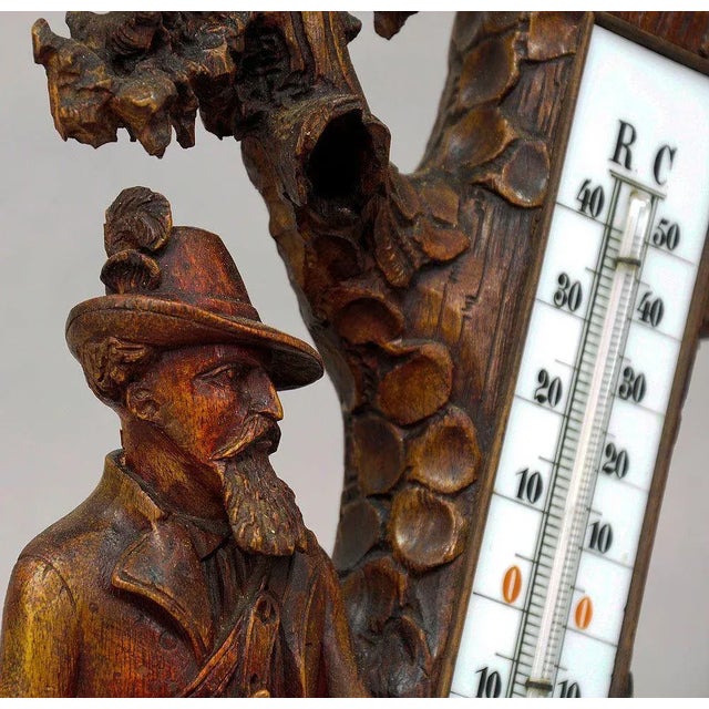 A Black Forest thermometer with impressive carved hunter and staghound standing on a naturalistic carved base by a stump....