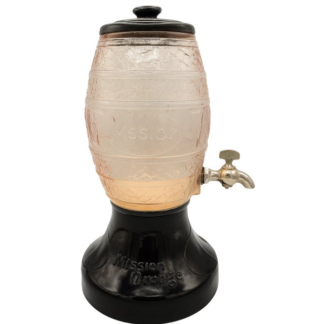 A striking Depression-era Mission Orange soda fountain dispenser dating to the 1930s. The textured pink glass barrel is...