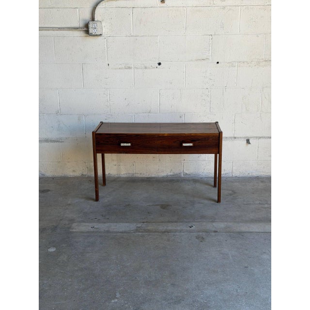 This minimalist hallway console table features a long rectilinear top flanked by slightly raised side lip borders. Two...