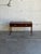This minimalist hallway console table features a long rectilinear top flanked by slightly raised side lip borders. Two...