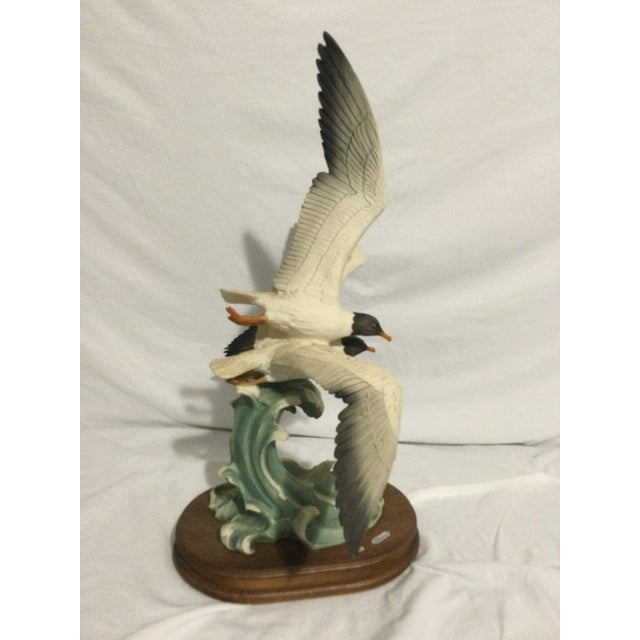 Vintage bird sculpture featuring a dynamic coastal scene with two birds in flight over stylized waves. The piece is...