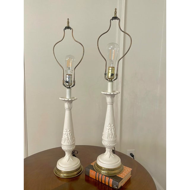 A pair of Neoclassical Revival style ceramic table lamps have a porcelain relief depicting dancing nymphs with floral and...