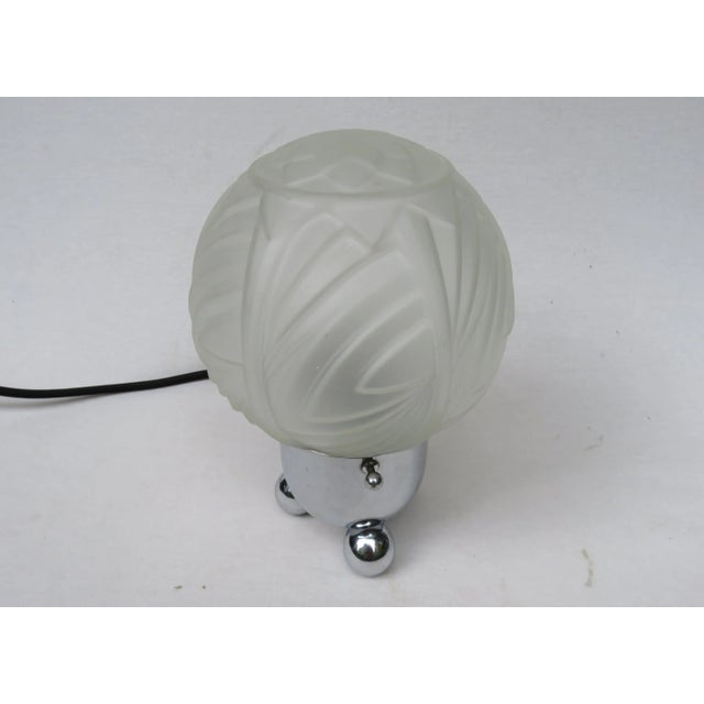 An extraordinary small table lamp from the Art Deco period. The lamp stands on 3 ball feet. The base is chrome plated. The...