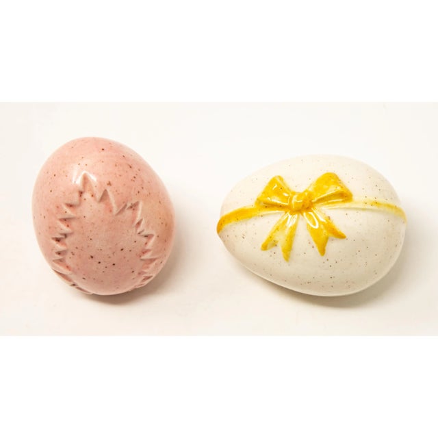 Offering a pair of ceramic glazed eggs. One is pink with speckles with a leaf stamped in the side. The other egg is cream...