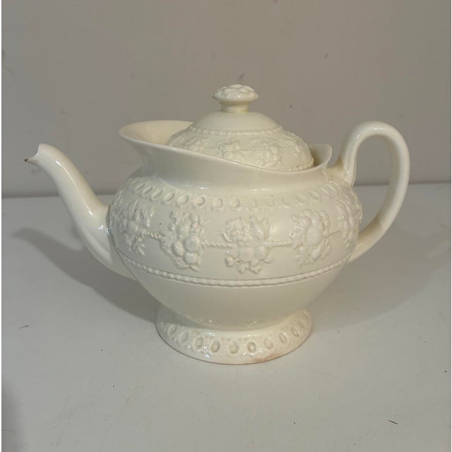 An elegant vintage Wedgwood Wellesley creamware teapot featuring embossed floral garlands, fruit swags, and beaded borders...
