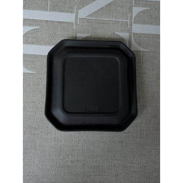 This is a Wedgwood black jasperware fluted square pin dish featuring a white Neoclassical relief design. Features a fluted...