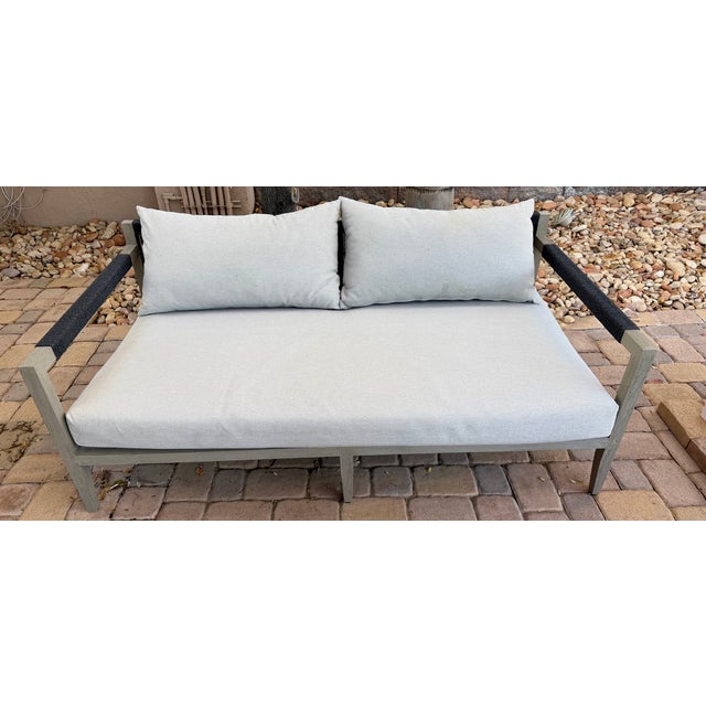 A refined Four Hands outdoor loveseat featuring a clean, modern silhouette upholstered in a versatile stone grey...