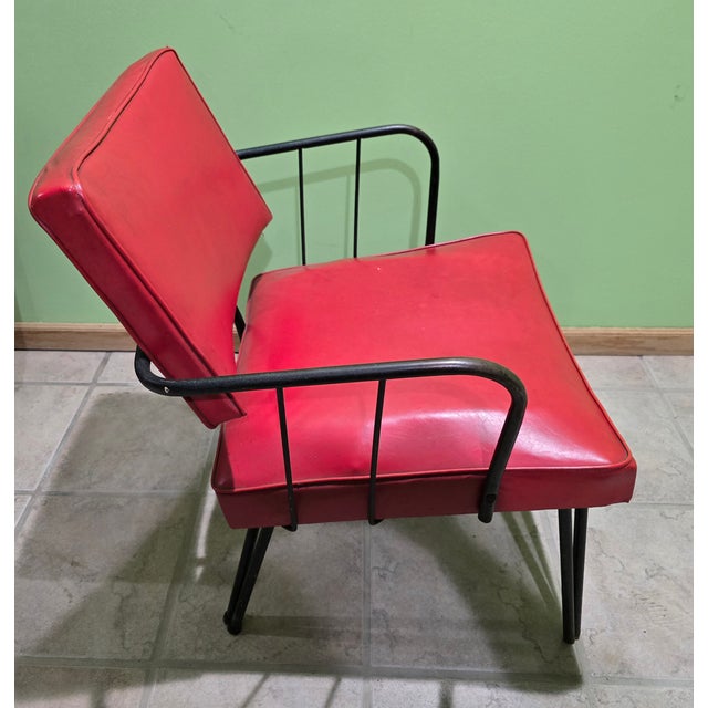 This mid-century modern chair features a striking red vinyl seat and backrest with a sturdy black metal frame. Its bold...