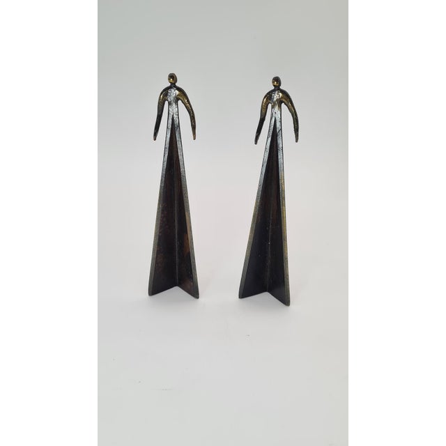 The bronze sculptures depict stylized figures on pyramidal bases and are referred to as figural or brutalist sculptures....