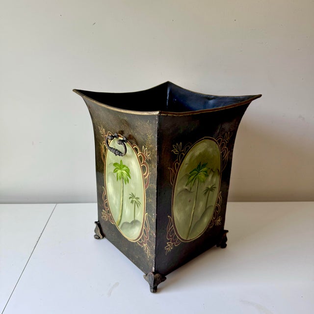 Vintage hand painted palm tree footed meta tole wastebasket. This piece is in a black base with gold and bronze details,...