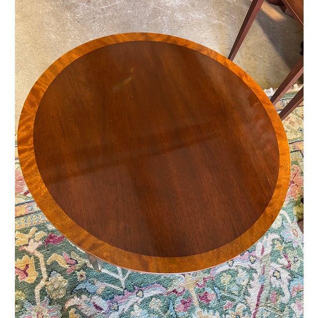 Round mahogany side table by Baker Furniture. Features heavily inlaid foliate motifs around the apron and drawer fronts....