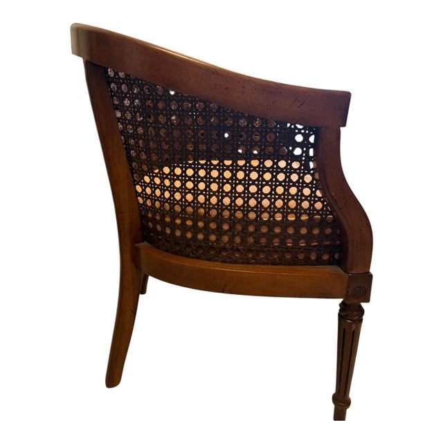 An elegant vintage barrel-back armchair combining sculptural carved wood with intricate woven cane. The gracefully curved...