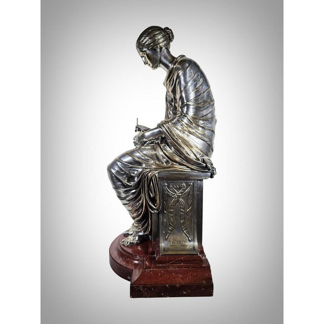 Behold this magnificent bronze sculpture depicting a possibly Greek lady seated, delicately holding a pencil. Crafted with...