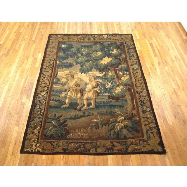A Flemish tapestry from the 17th century, incorporating verdure and rustic elements, with two rustic men walking in a...