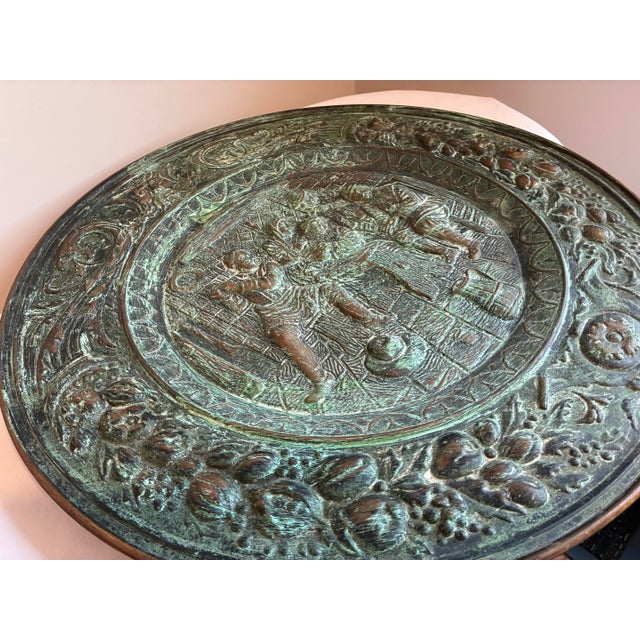 An oversized 22.5-inch antique copper repoussé decorative charger / wall plaque featuring a Dutch tavern scene. The deeply...