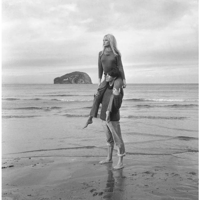 Iconic French actress Brigitte Bardot is carried by a male friend over the wet sand on the beach. 16" x 20" print Silver...
