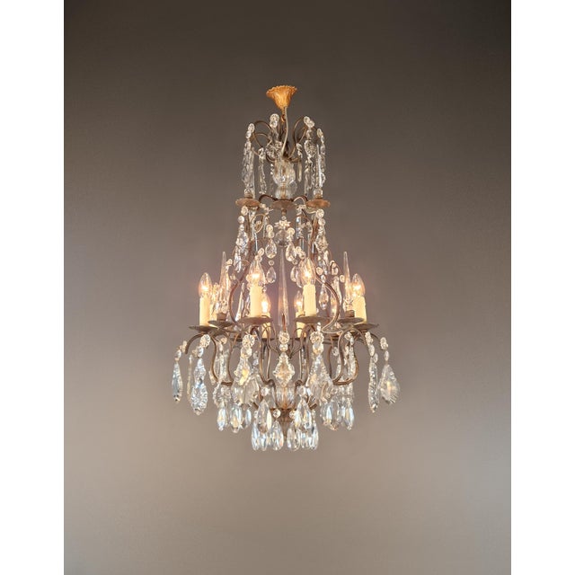 This antique French chandelier captivates with its sleek, tiered design featuring curved brass arms and a varied...