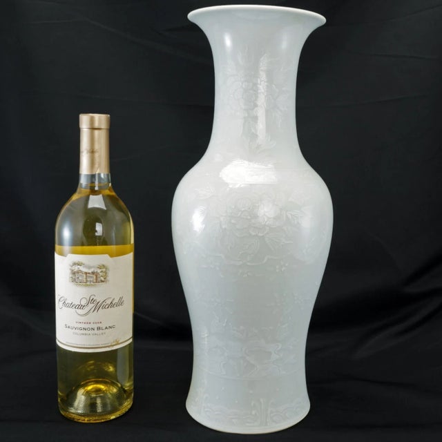 A large white on white Japanese porcelain vase with subtle designs of peonies above stylized waves at the foot. The vase...