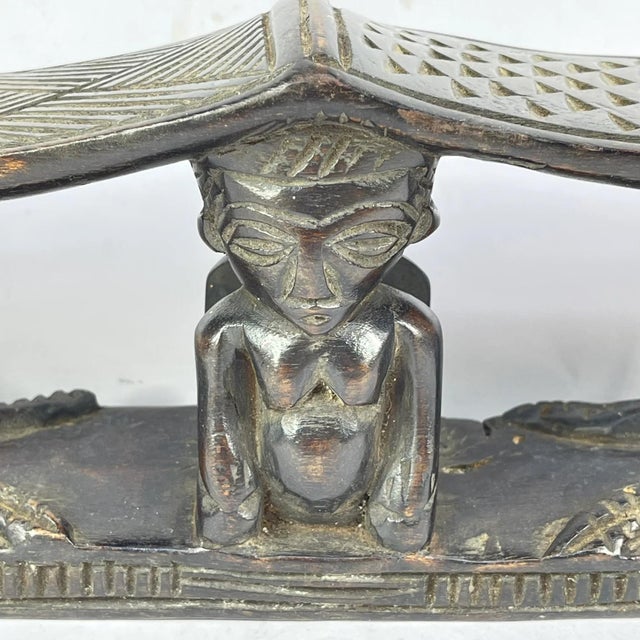 A carved double headrest from the Songye people is a sculptural sleeping support traditionally used in the savanna regions...
