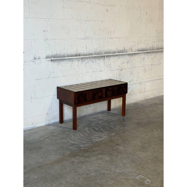 This console features a rectangular silhouette elevated by straight legs. The striking top showcases a geometric tile...