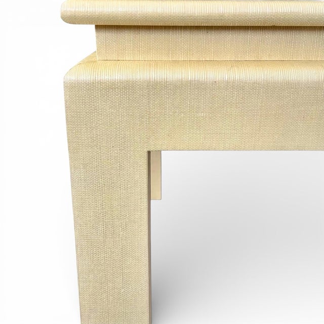 A lovely cocktail table in a champagne-tone yellow woven material resembling grasscloth or linen wrapped over solid wood...