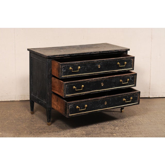 A French Neoclassical period painted wood commode with brass trimmings from the early 19th century. This antique chest...