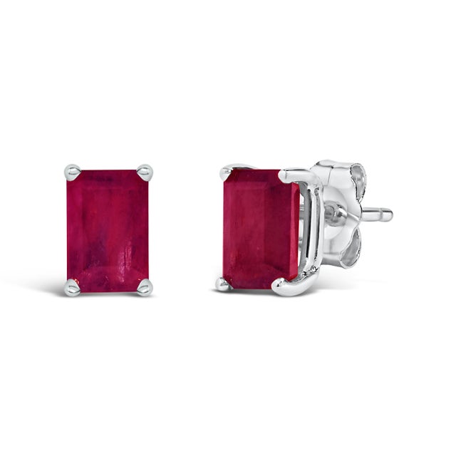 Immerse yourself in the timeless elegance of these stud earrings, each boasting a lustrous 6x4mm emerald-cut red ruby,...