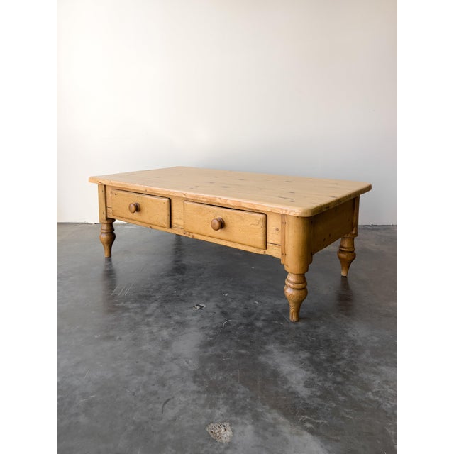 An antique English pine coffee table with a reclaimed pine top and turned legs. Drawers with wooden knobs for extra...