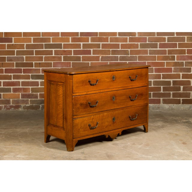 A French walnut commode from the 18th century with three drawers, carved apron and ornate hardware. This 18th-century...