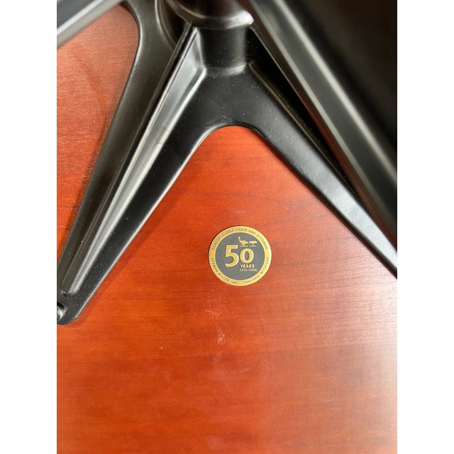 50th anniversary edition Herman Miller Eames chair and ottoman, featuring low-sheen black leather and cherry wood frame....