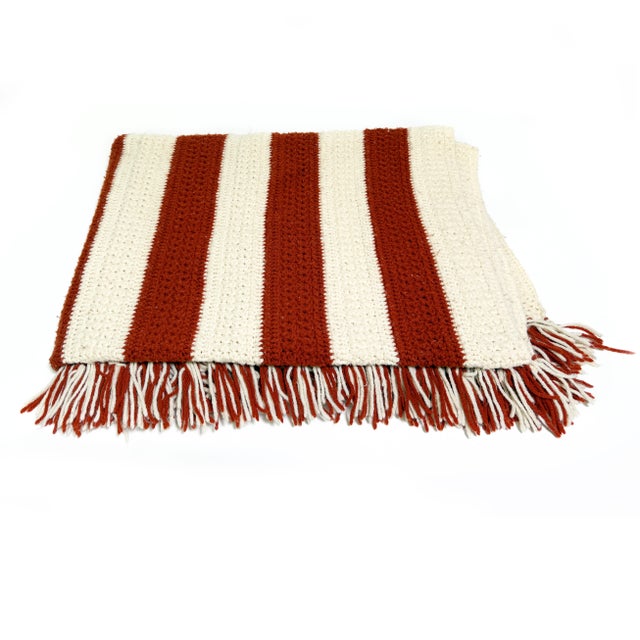 A charming vintage handmade crochet throw blanket featuring classic burnt orange and cream stripes with hand-tied fringe...