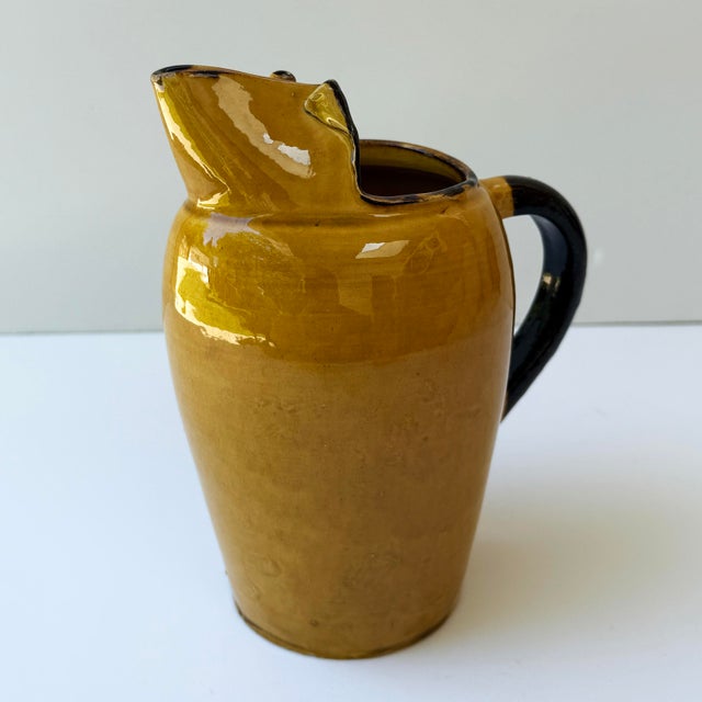 A charming mid-century French stoneware pitcher from the celebrated pottery town of Vallauris, featuring a rich ochre-...