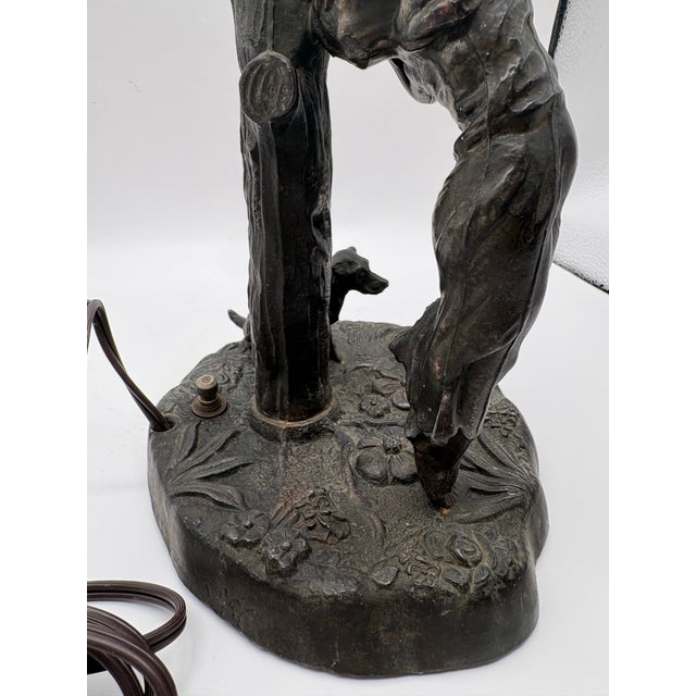 Cast Bronze table lamp featuring a women, tree stump and dog with beautiful pink glass ruffled shade designed to replicate...