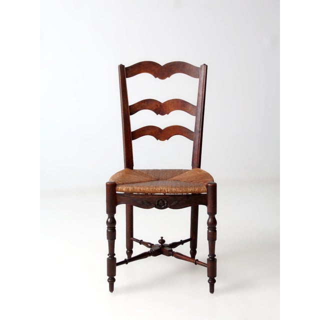 An antique French provincial ladderback chair featuring softly shaped slats, turned legs, and a handwoven rush seat in a...