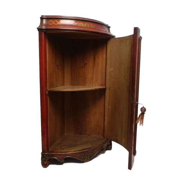 Wonderful red lacquered corner cabinet (encoignure) with gilt highlighted chinoiserie scene, standing on leaf and scroll...