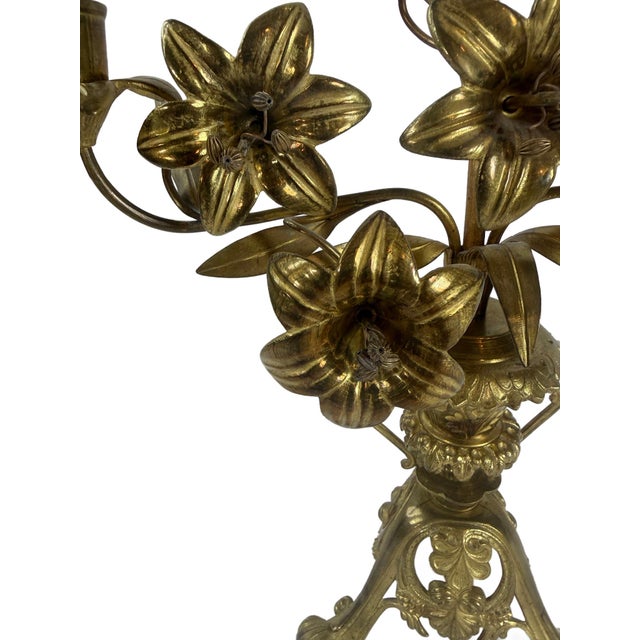 This is an antique French brass candelabra featuring an elaborate arrangement of sculpted lilies and foliage rising from a...