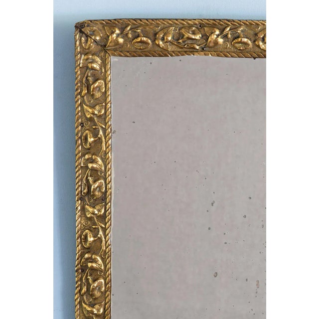 An elegant 18th-century French brass repoussé mirror, featuring a rectangular frame decorated with a refined frieze of...